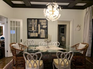 A dining area with a glass table, white chairs, a chandelier, and a large abstract painting on the wall. - Curated boutique stay in a 1920s English bungalow. Modern twist on a classic! (Waco)