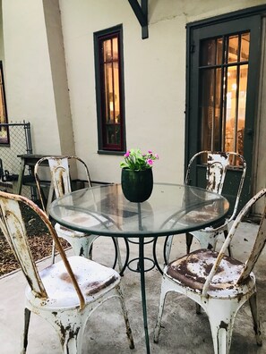 A round glass table with a black pot of flowers, surrounded by four white chairs with metal frames. - Curated boutique stay in a 1920s English bungalow. Modern twist on a classic! (Waco)