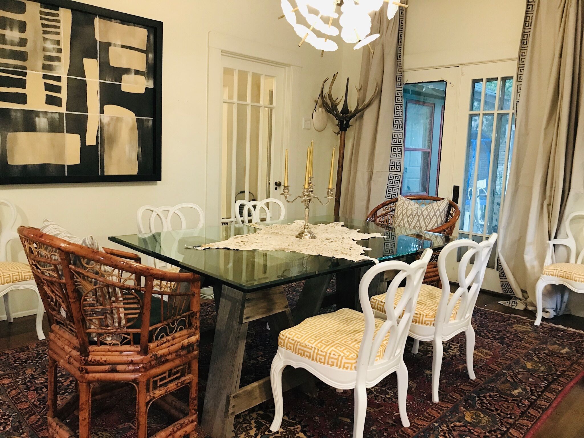 Comedor con mesa de vidrio rodeada de sillas blancas, un candelabro y un adorno en la pared.