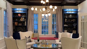 Una sala de estar moderna con una mesa redonda, dos sillones blancos, un sofá y una estantería.