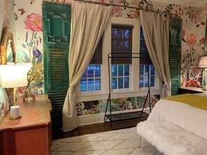 A bedroom with a bed, a window with curtains, a lamp, and floral wallpaper. - Curated boutique stay in a 1920s English bungalow. Modern twist on a classic! (Waco)