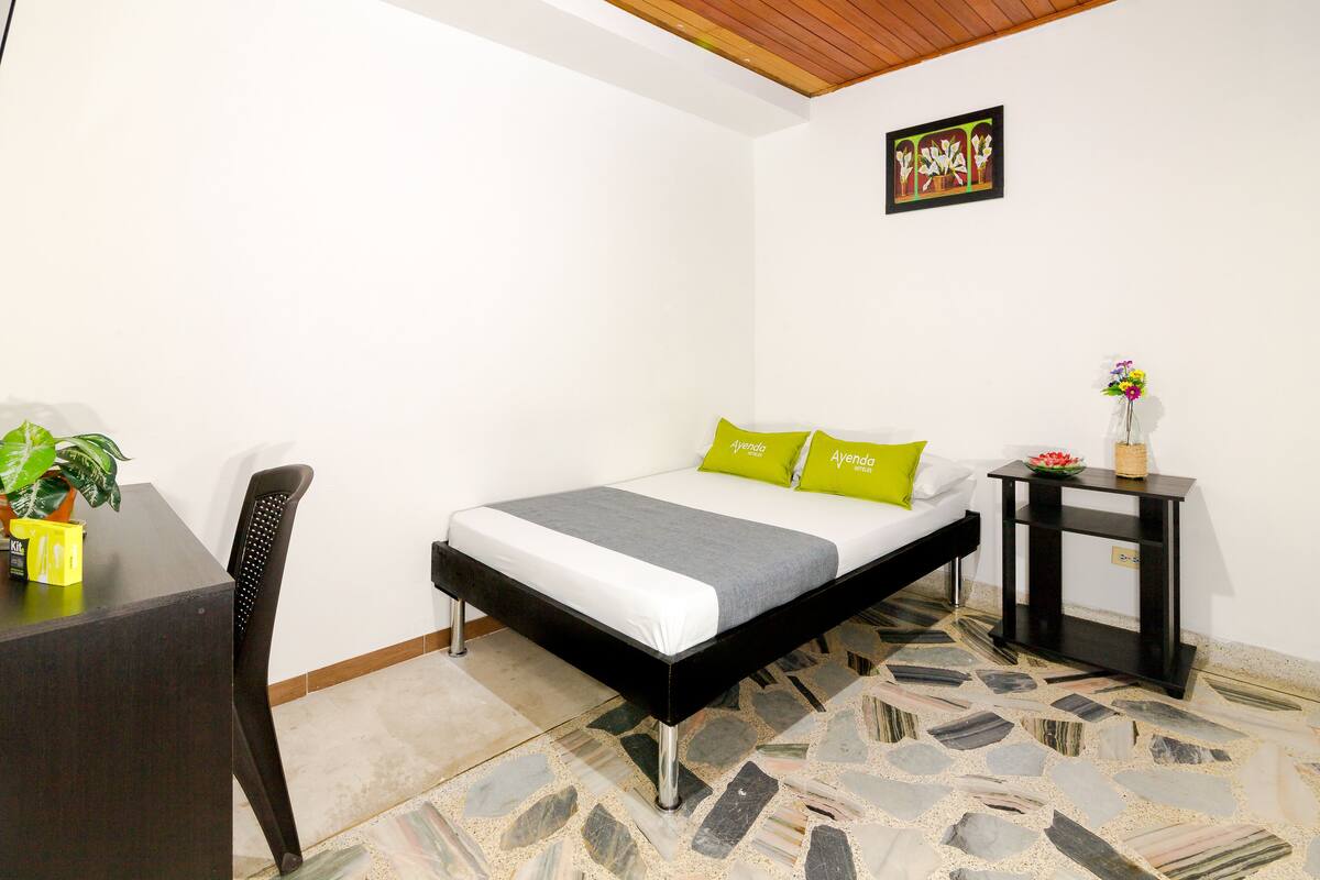Une chambre à coucher avec un lit, une table de chevet, une chaise, une plante en pot et un sol carrelé.