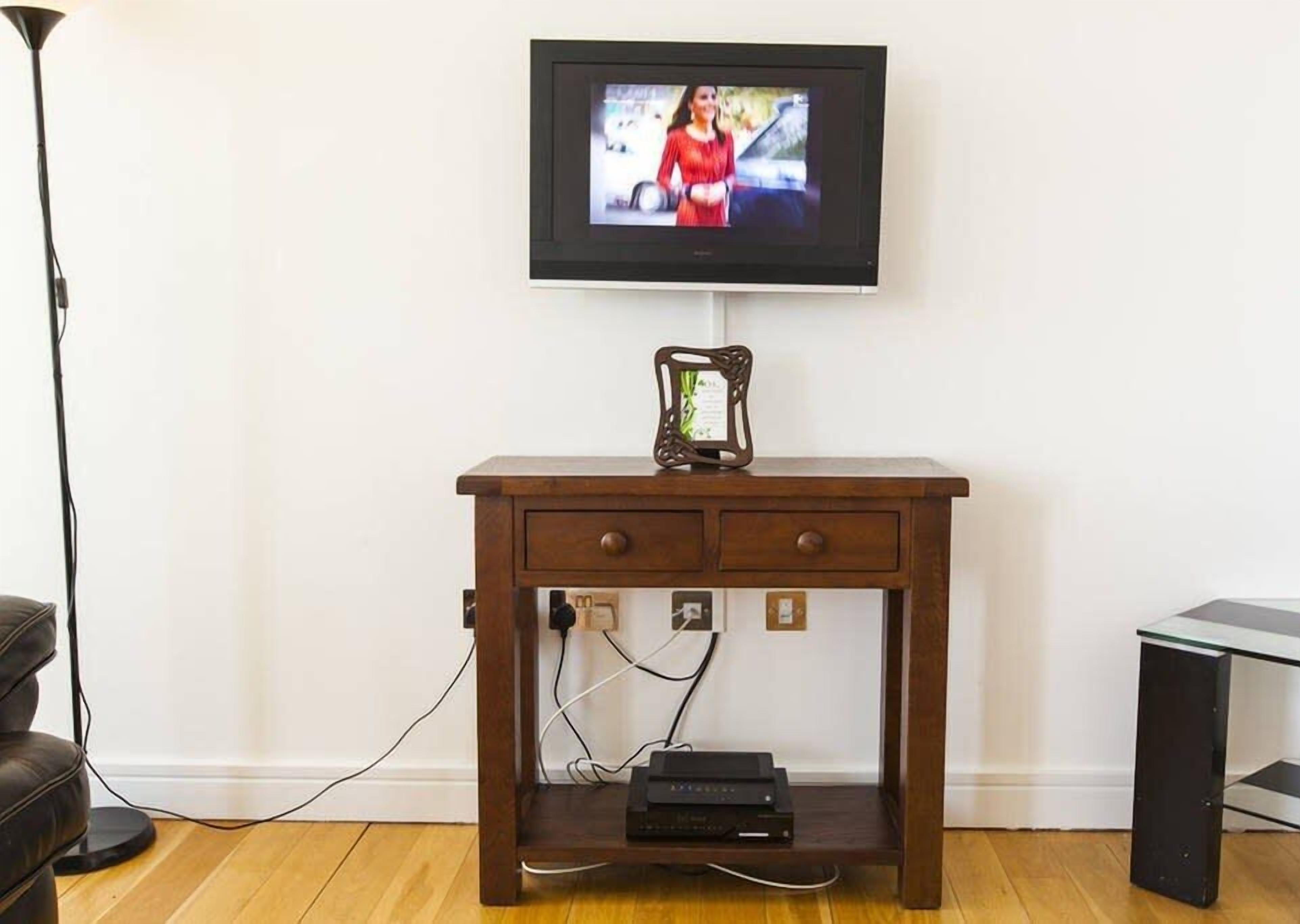 Um suporte de TV de madeira com uma televisão de tela plana montada acima, uma mesinha com um objeto decorativo e um sistema de organização de cabos.