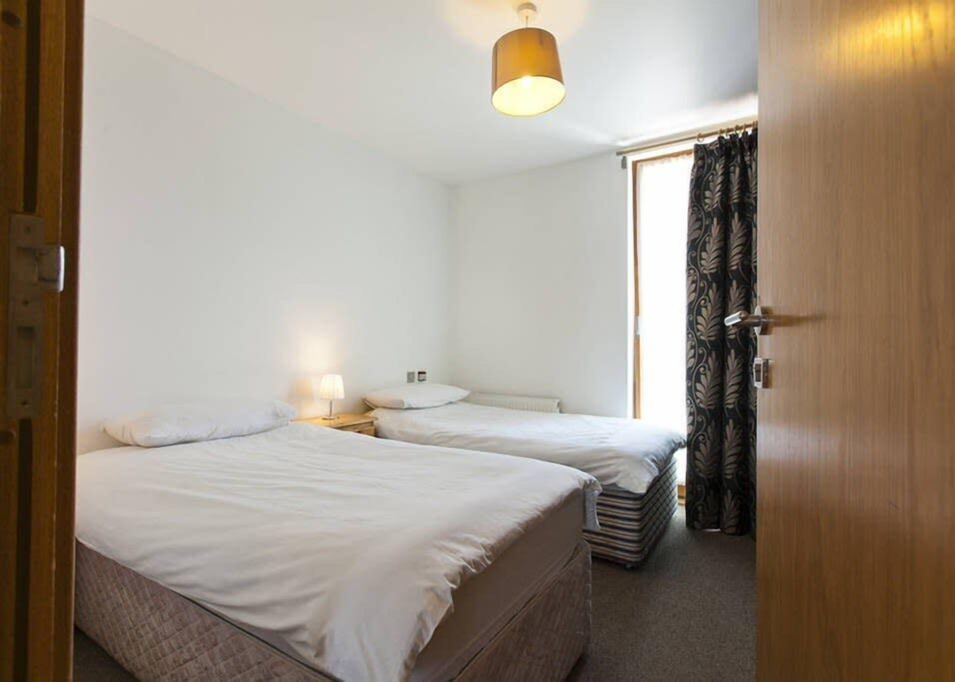 A room with two beds, a wooden door, and a window with curtains.