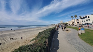 A beachside promenade with a paved walkway, beach, and residential buildings in the background.