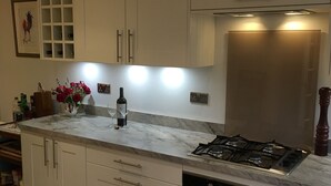 A modern kitchen with white cabinets, a marble countertop, a built-in oven, and a stainless steel range hood. - Quaint cottage in the heart of the village in the heart of Scotland. (Aberfeldy)