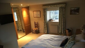 A bedroom with a bed, a chair, a window with curtains, a radiator, and a painting on the wall. - Quaint cottage in the heart of the village in the heart of Scotland. (Aberfeldy)