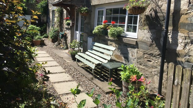 A stone building with a wooden bench and potted plants. - Quaint cottage in the heart of the village in the heart of Scotland. (Aberfeldy)