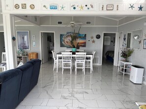 A spacious living area with a dining table, white chairs, a ceiling fan, and a large painting. - BEACH FRONT ISLAND COTTAGE 3 BEDROOM,1 BA  PETS MUST BE DECLARED WHEN BOOKED. (Sargent)