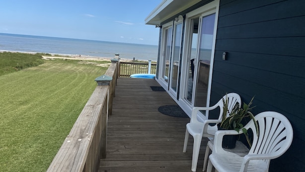 Une terrasse en bois avec des chaises en plastique blanches, donnant sur une plage et l’océan.