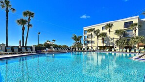 A clear blue pool with lounge chairs, palm trees, and a building with balconies. - Land's End #403 Building 3 - Beautiful Updates/awesome BAY View! (Treasure Island)