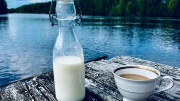 A glass milk bottle and a white cup on a wooden surface by a lake.