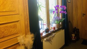 A room with a wooden door, a window with a view of greenery, a radiator, and a teddy bear on a chair. - Charming 1-bed Studio in Avesta (Avesta)