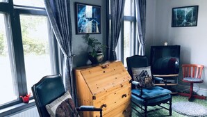 A cozy living room with a wooden dresser, two chairs, a television, and large windows with curtains. - Charming 1-bed Studio in Avesta (Avesta)