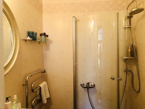 A bathroom with a glass shower enclosure, a towel rack, a shelf with toiletries, and a mirror.
