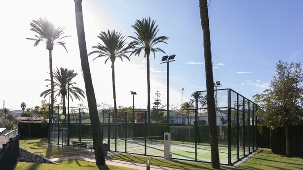 A tennis court with a fence, benches, and palm trees. - Brisas B2, 2 bedrooms, beach at 50m, by Bookindenia (Dénia)