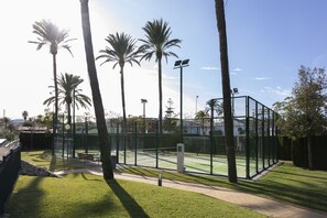 A tennis court with a fence, benches, and palm trees.