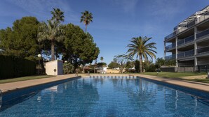 A swimming pool with tiled flooring, surrounded by palm trees and a multi-story building with balconies. - Brisas B2, 2 bedrooms, beach at 50m, by Bookindenia (Dénia)