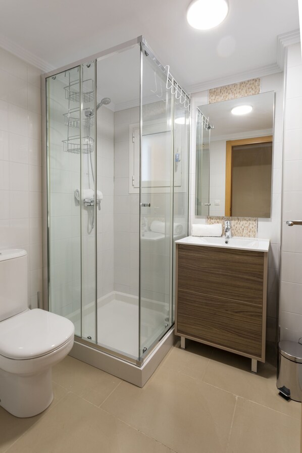 A modern bathroom with a glass-enclosed shower, a white toilet, and a wooden vanity with a mirror above it.