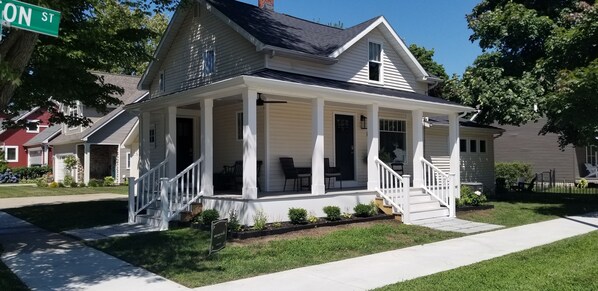 Stunning two-story house with a covered porch and a front staircase, set amidst a beautifully maintained lawn and sidewalk.