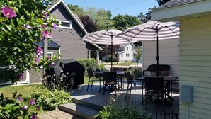 Un patio con mobiliario exterior y sombrillas, rodeado de un jardín y casas.