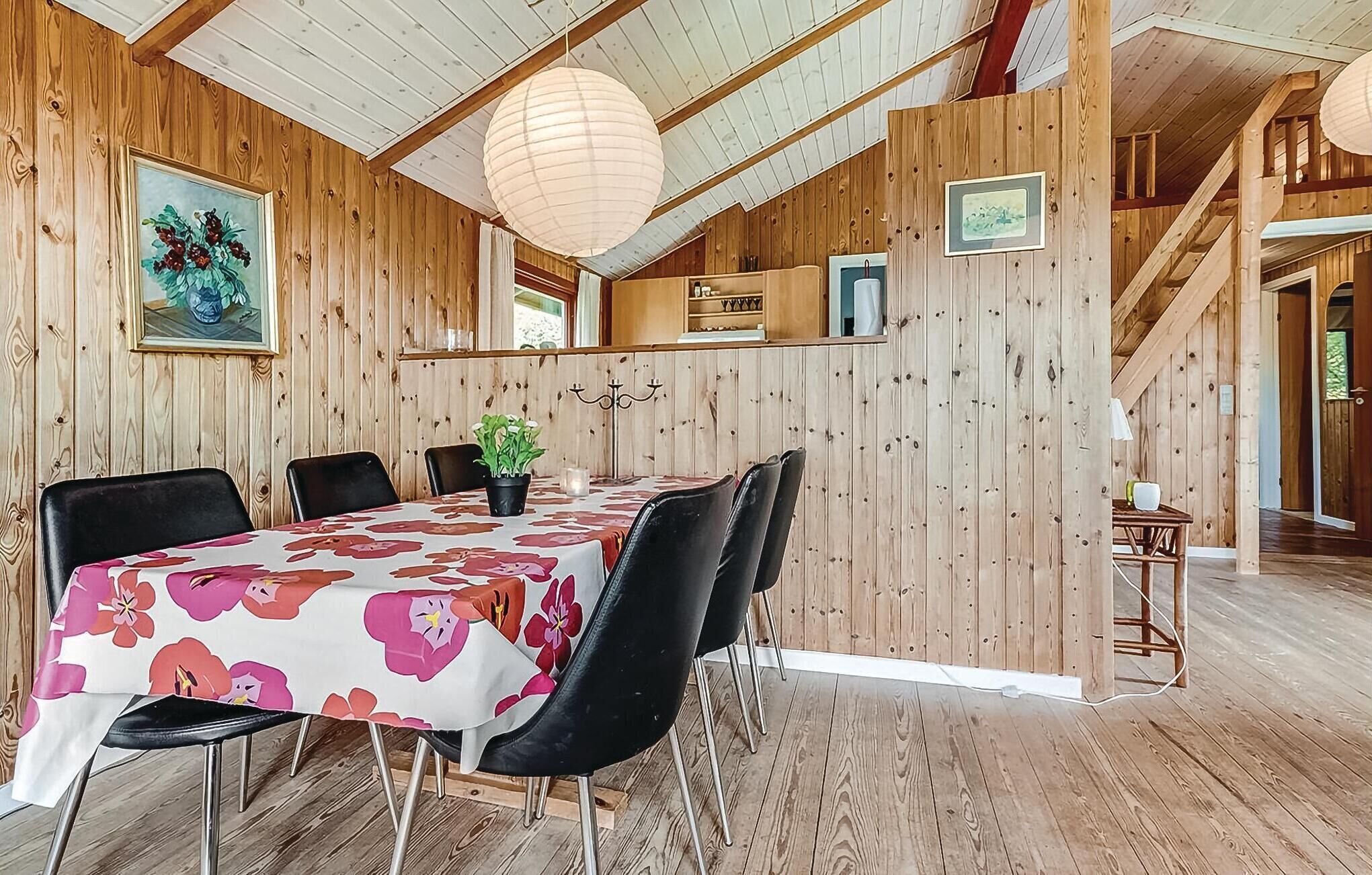 Ein Essbereich mit Holzvertäfelung, einem Tisch mit floralem Tischläufer, schwarzen Stühlen und einer hängenden Leuchte.