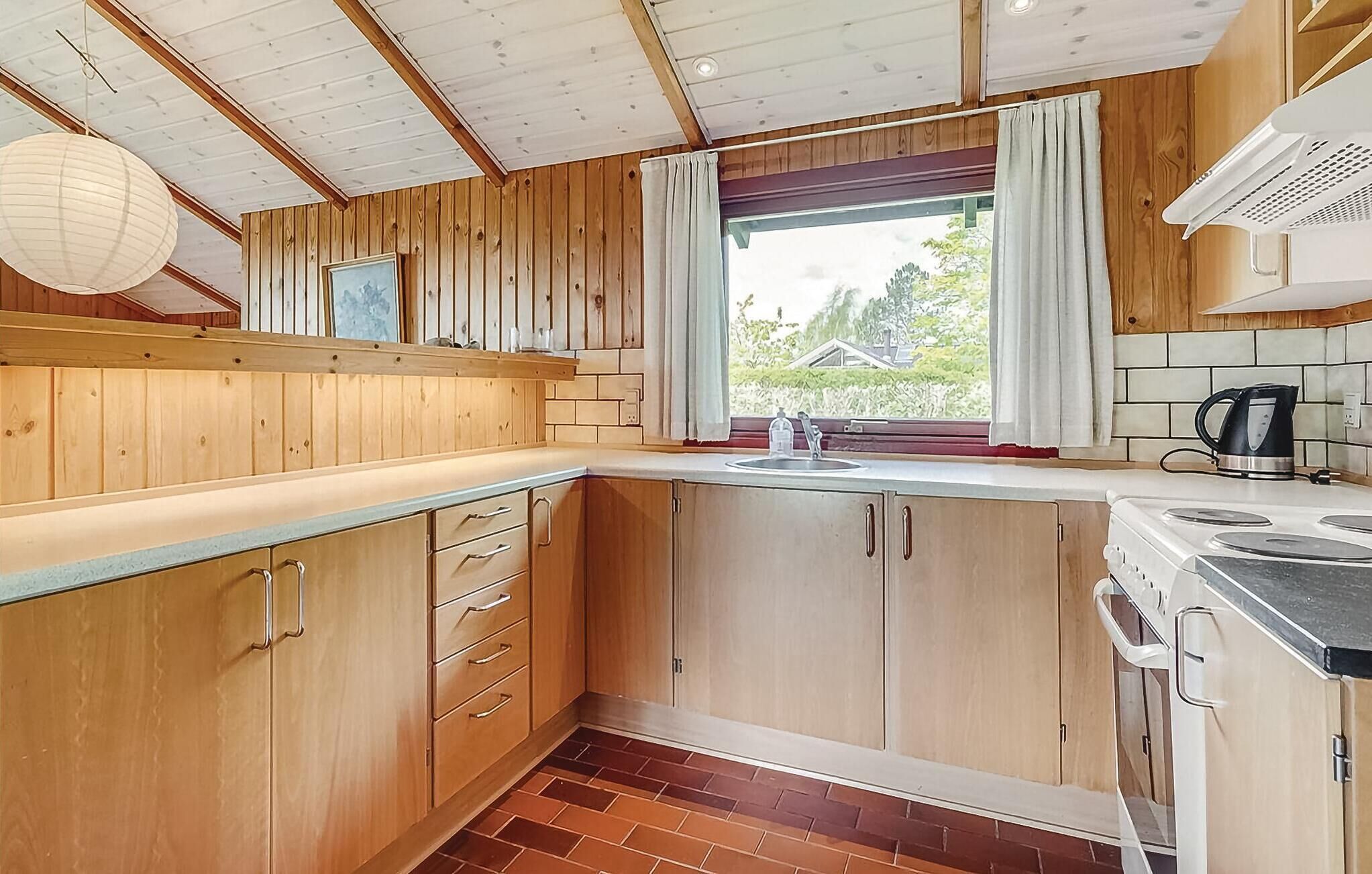 Eine Küche mit Holzausstattung, einem Spülbecken, einem Herd und einem Fenster mit Vorhängen.