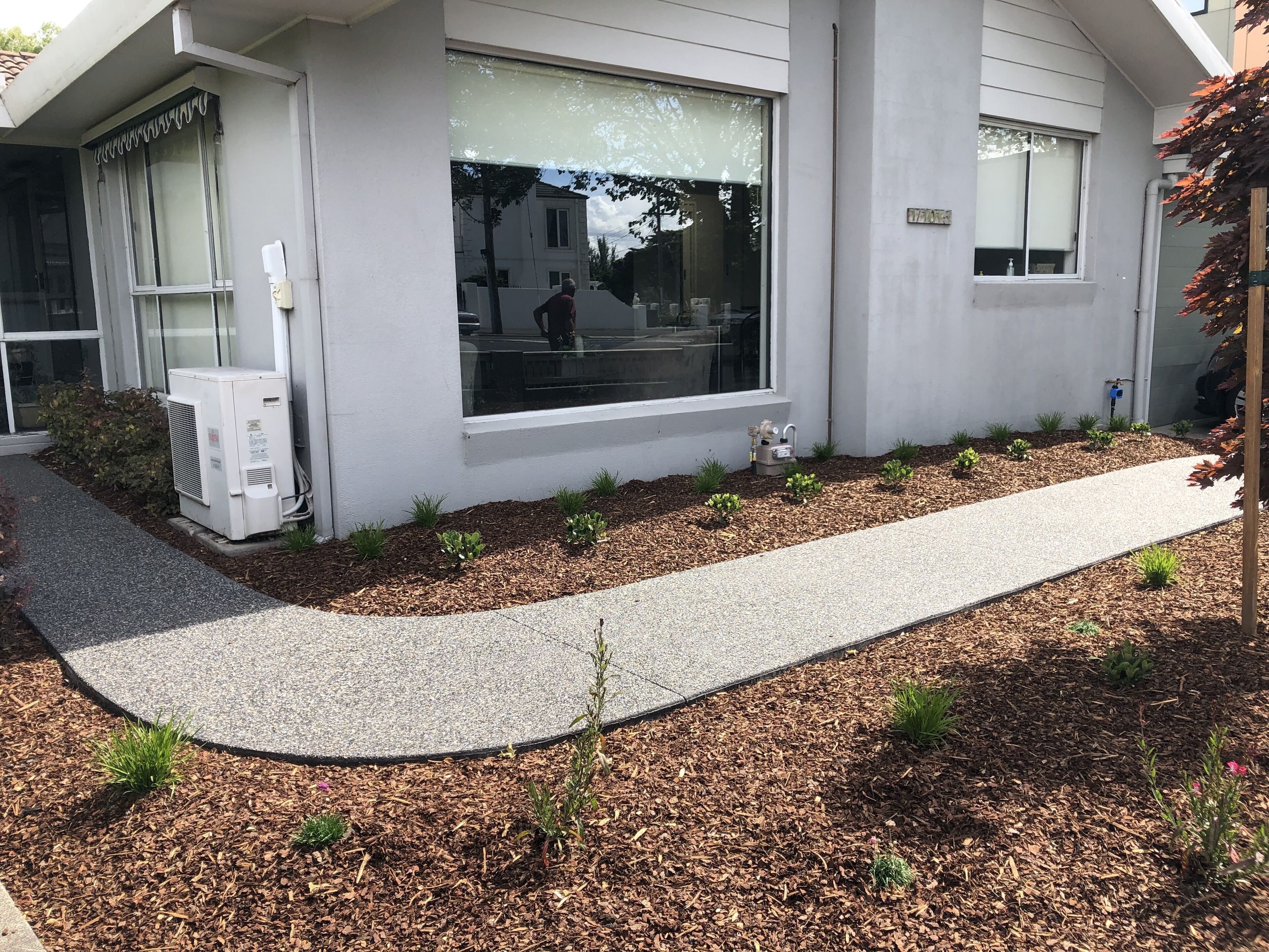 A modern building with a pathway, small plants, and an air conditioning unit.