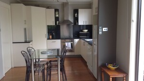 Une cuisine compacte avec des meubles blancs, une hotte en acier inoxydable, un four à micro-ondes et une petite table en bois sur laquelle se trouve un saladier.