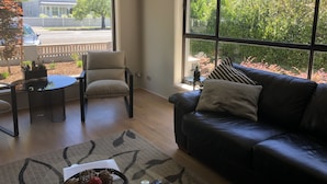Un salon moderne avec un canapé en cuir, une table à manger avec des chaises et de grandes fenêtres donnant sur l’extérieur.