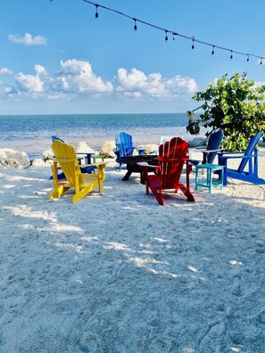 A beach with colorful Adirondack chairs and a string of lights.