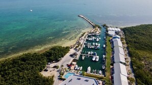 An aerial view of a coastal marina with boats docked, a pier extending into the water, and a building adjacent to the marina. - Welcome to Paradise! (Key Largo)