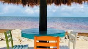 A beachside table with a thatched roof umbrella, two chairs, and a view of the ocean. - Welcome to Paradise! (Key Largo)