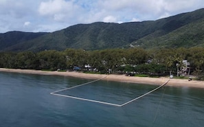 Una spiaggia con acque cristalline, una riva sabbiosa e colline verdi sullo sfondo.