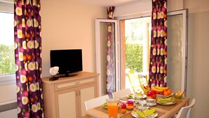 Un comedor con una mesa lista para el desayuno, un televisor en un mueble y cortinas con un diseño circular.