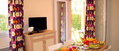 A dining area with a table set for breakfast, a television on a cabinet, and curtains with a circular pattern.