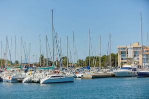 A marina with multiple boats docked, a building with balconies, and a clear sky.