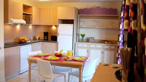 A modern kitchen with wooden cabinets, a dining table set for two, and a refrigerator.