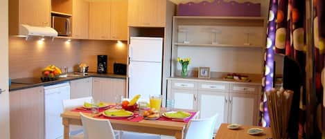 A modern kitchen with wooden cabinets, a dining table set for two, and a refrigerator.