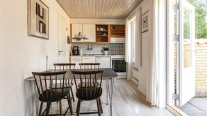 Ett kompakt kök med vita skåp, ett matbord med fyra stolar och utsikt över omgivningen genom en glasdörr.