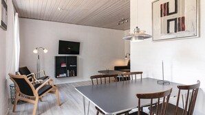 Ett modernt matområde med ett långt bord, trästolar, en platt-TV och en hängande lampa.
