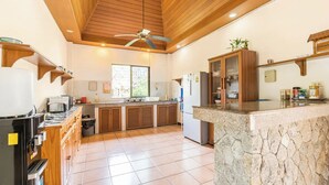 A modern kitchen with wooden cabinets, a stone island, and a ceiling fan. - Baan Coconut (Choeng Thale)
