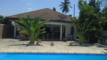 A house with a tiled roof, a swimming pool, and tropical plants.