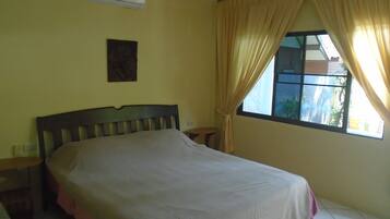 A bedroom with a bed, an air conditioner, a window with curtains, and a small table.