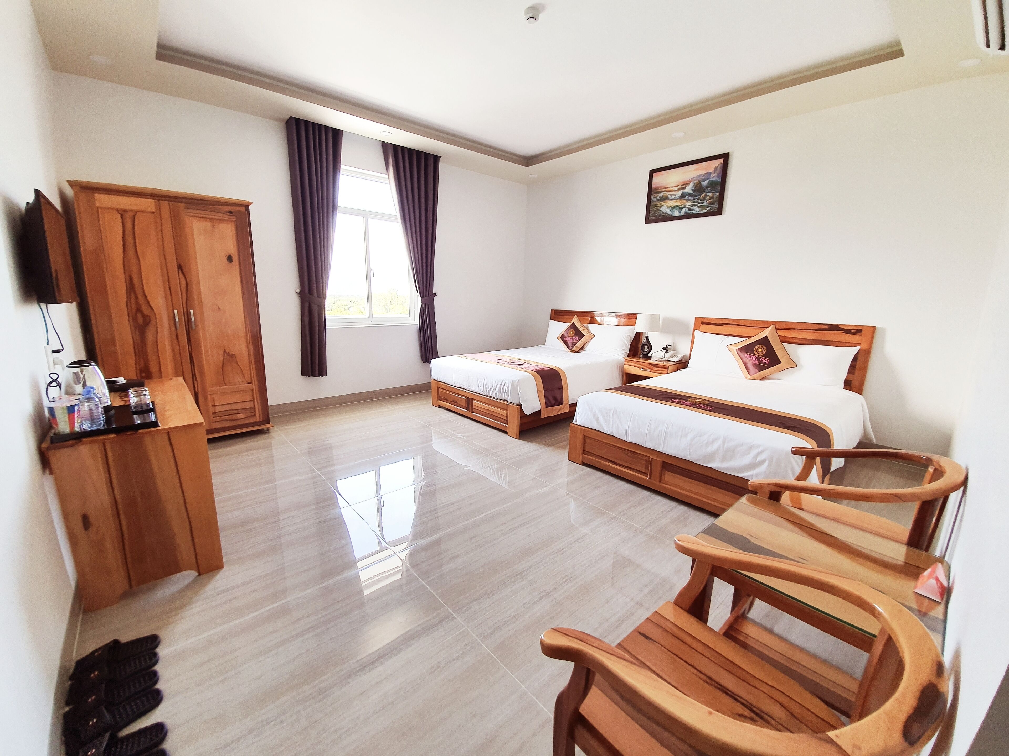 A hotel room with two wooden beds, a wooden wardrobe, a desk with a chair, and a large window with curtains.