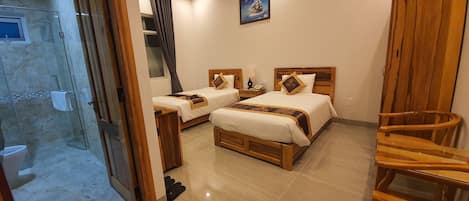 A hotel room with two beds, a wooden chair, a shower area, and a painting on the wall.