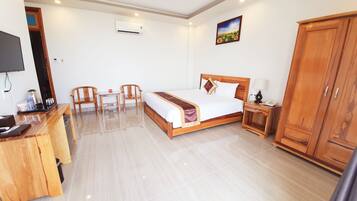 A hotel room with a bed, bedside table, lamp, wardrobe, desk with chairs, and a television.