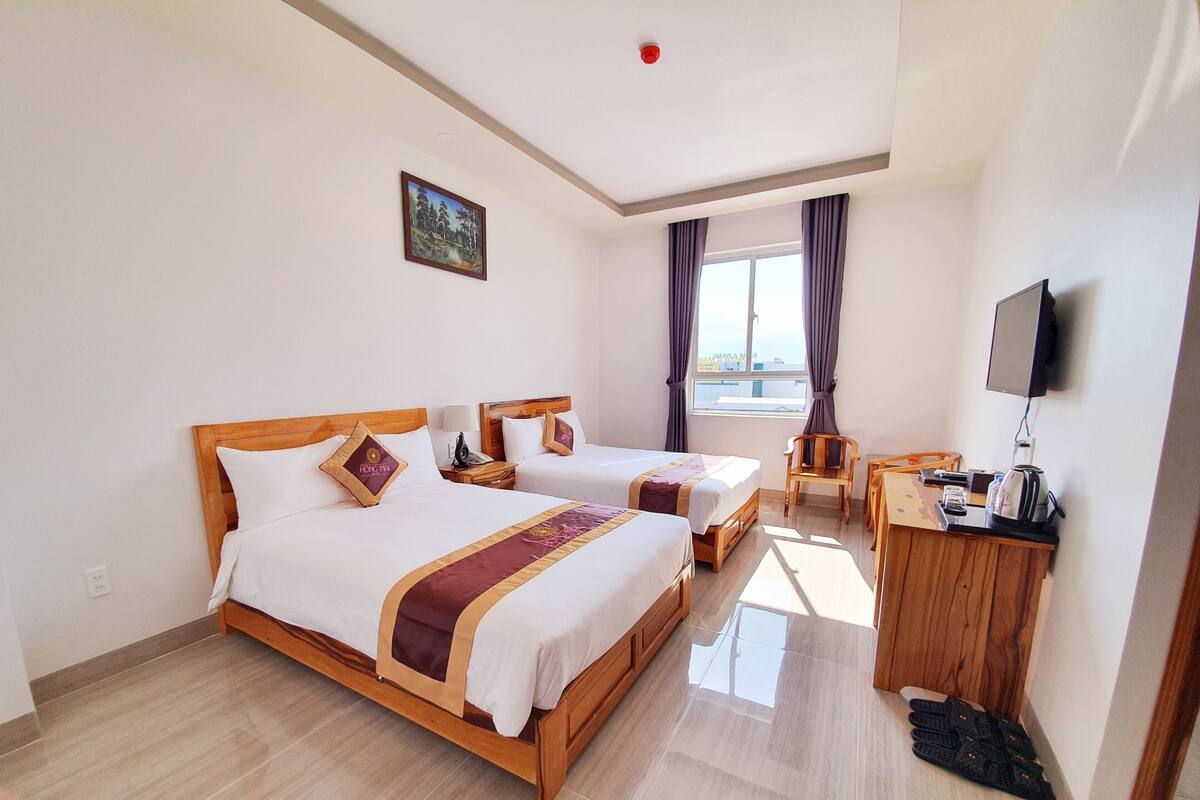 Ett hotellrum med två sängar, ett skrivbord, en stol, en tv och ett fönster med gardiner.