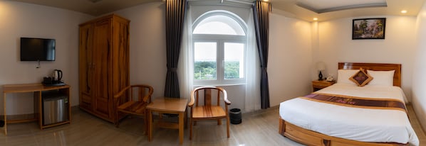 A hotel room with a bed, a desk, a television, a wardrobe, and a window with curtains.
