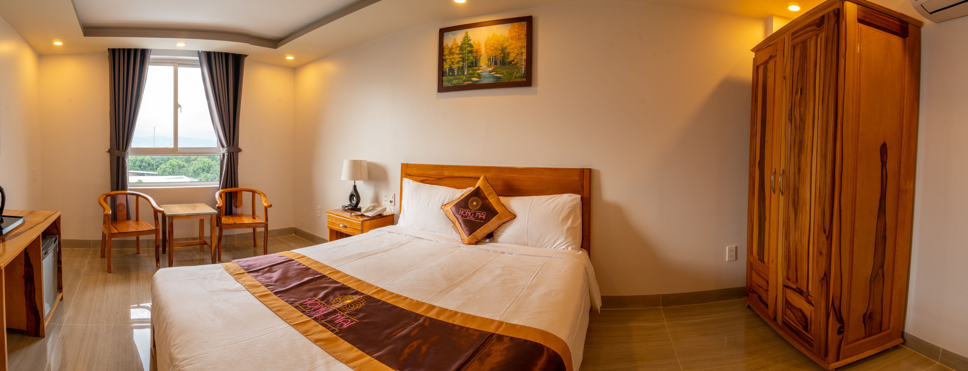 A hotel room with a bed, a desk, a chair, a wardrobe, and a painting on the wall.